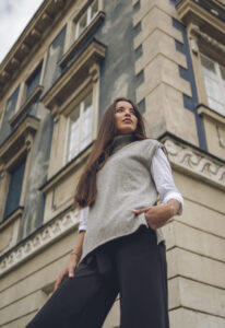 Zdjęcie kobiety w centrum miasta, która ubrana jest w szary sweter bez rękawów i czarne spodnie